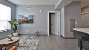 A modern hotel room with a large window, a round wooden table with a globe, a potted plant, a painting of a cityscape, and a door leading to another room. - Home Away from Home Near Downtown (Columbus)