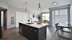 A modern kitchen with a central island, built-in appliances, and pendant lighting. - The South Campus Suite (Columbus)