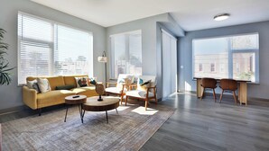 A spacious living room with a sofa, chairs, a coffee table, and a dining area with chairs. - The South Campus Suite (Columbus)