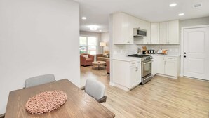 Une cuisine moderne avec des meubles blancs, un four encastré et un coin repas comprenant une table et des chaises en bois.