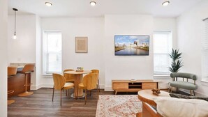 A modern living room with a dining area, a sofa, a TV, and a painting on the wall.