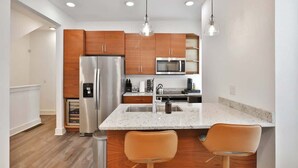 A modern kitchen with wooden cabinets, stainless steel appliances, a granite countertop, and pendant lighting.