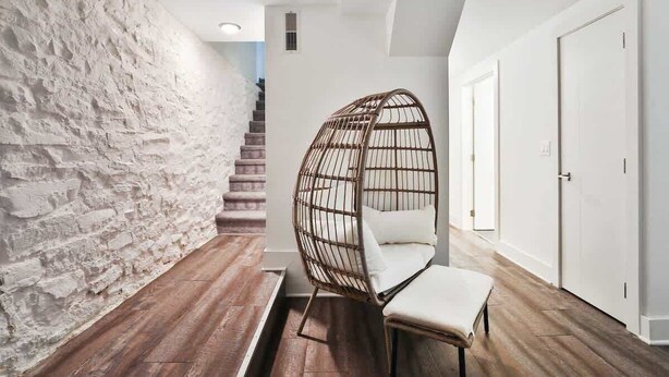 A modern interior with a stone wall, wooden flooring, a hanging chair, and a staircase.