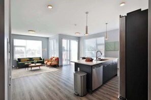 A modern kitchen with a central island, a dining area with a sofa and chairs, and a large window providing natural light. - The South Campus Loft (Columbus)