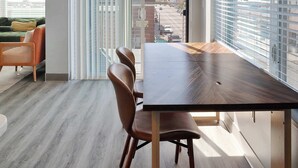 Zona pranzo moderna con tavolo e sedie in legno, ampie finestre con persiane e vista sulla città.