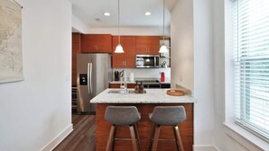 A modern kitchen with wooden cabinets, stainless steel appliances, and a central island with bar stools. - Contemporary Vintage Home (Near Downtown!) (Columbus)
