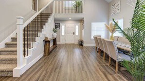 Un intérieur spacieux avec un escalier en bois, un coin repas comprenant des chaises et une table, ainsi qu’un panneau décoratif mural.