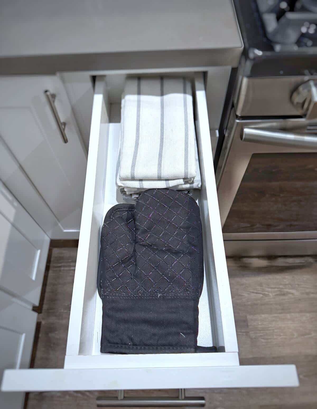 A kitchen drawer with a white towel and a black quilted bag.