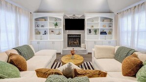 Un salon moderne doté d’une cheminée, de canapés blancs et d’étagères intégrées où sont exposés des objets décoratifs.