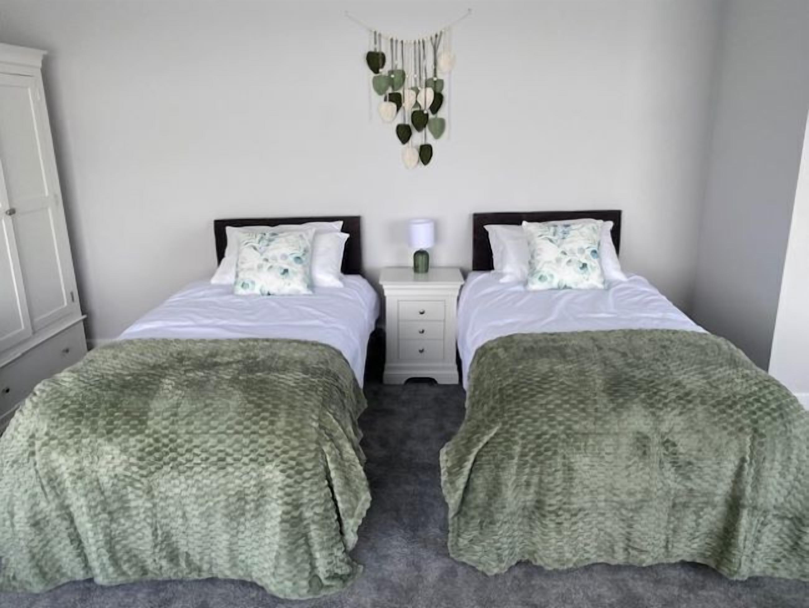 Habitación doble con dos camas, una mesita de noche, una decoración de macramé colgada en la pared y un armario.