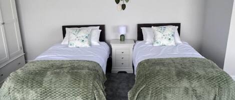Habitación doble con dos camas, una mesita de noche, una decoración de macramé colgada en la pared y un armario.