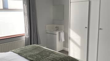A bedroom with a bed, a bedside table, a wardrobe, and a bathroom with a sink and mirror.