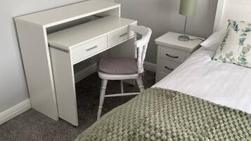 A bedroom with a bed, a desk, a chair, a nightstand, and a lamp.
