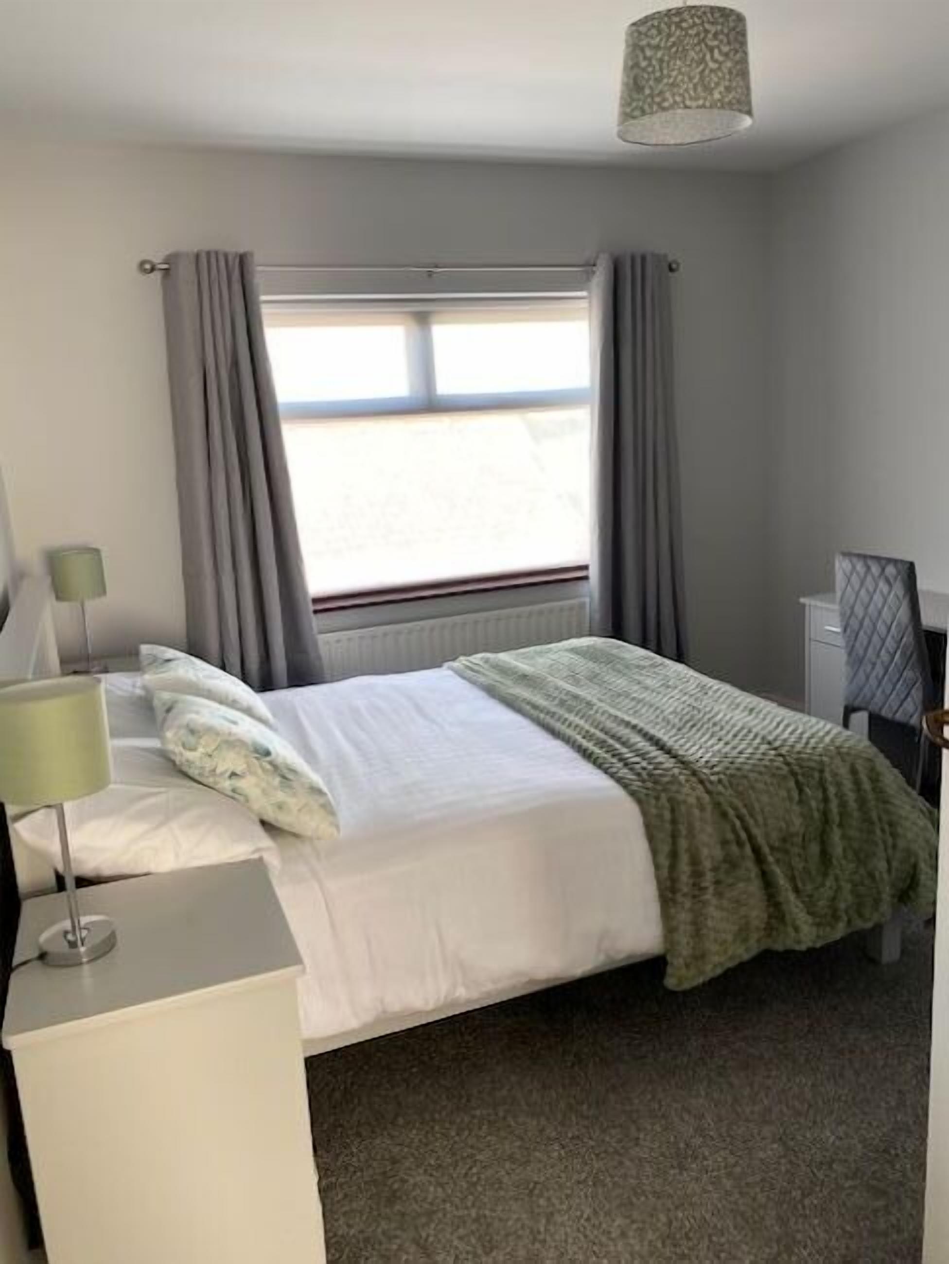 Una habitación de hotel con una cama, un escritorio, una lámpara y una ventana con cortinas.