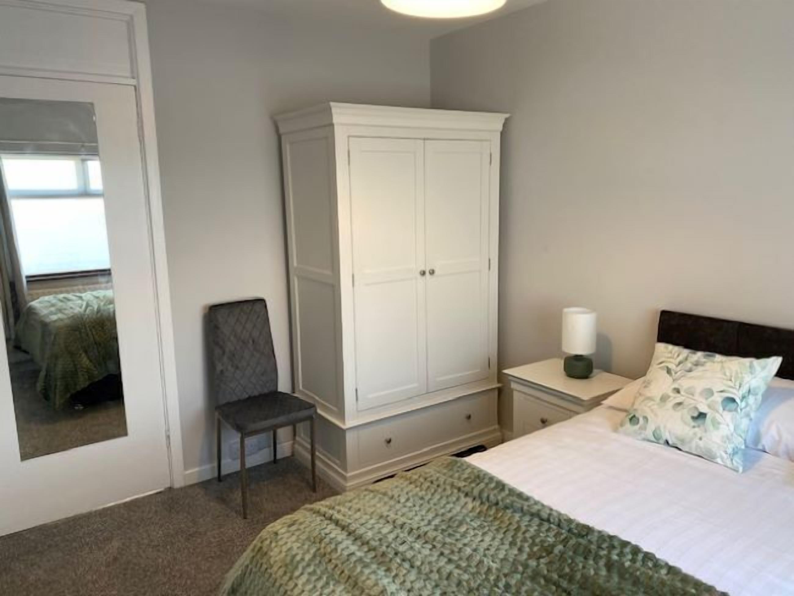 Ein Schlafzimmer mit Bett, Nachttisch, Stuhl, Kleiderschrank und Spiegel.