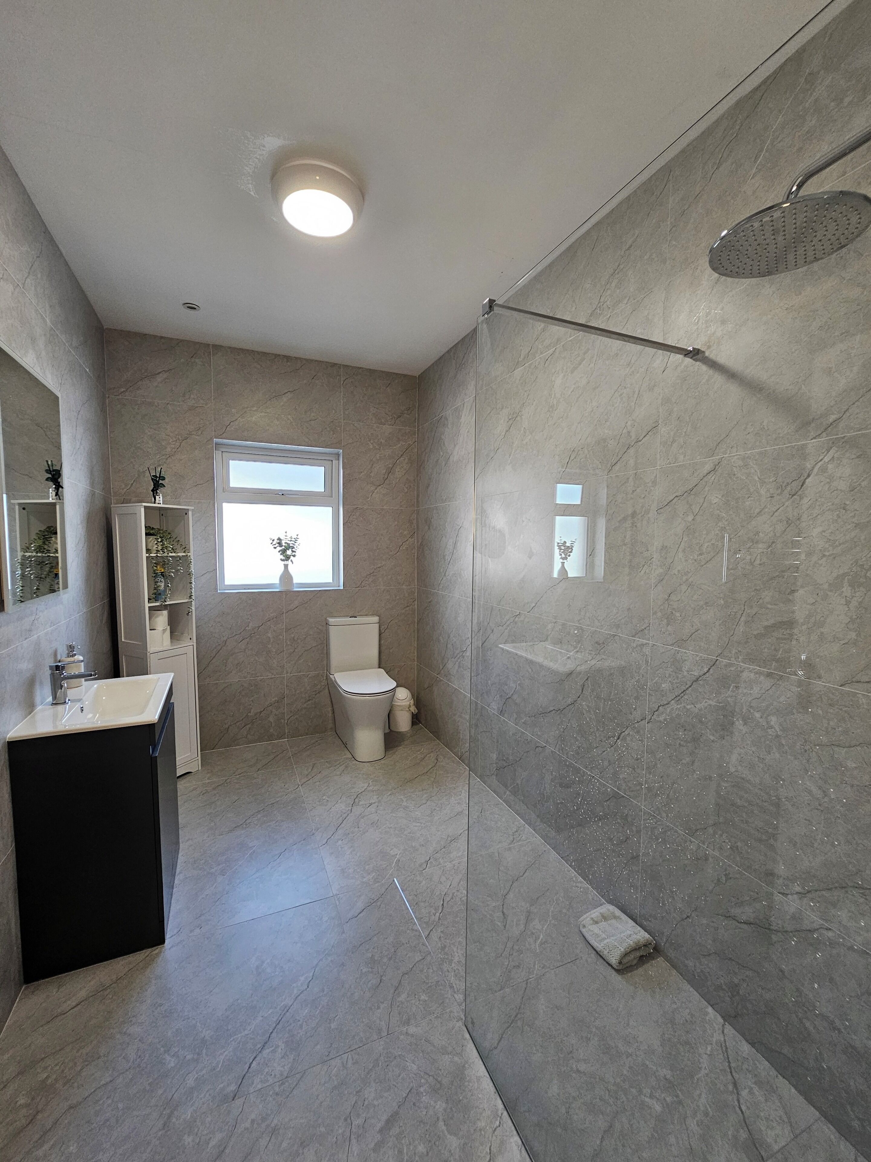 A bathroom with a shower, toilet, sink, and a window.