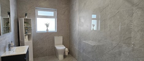 A bathroom with a shower, toilet, sink, and a window.