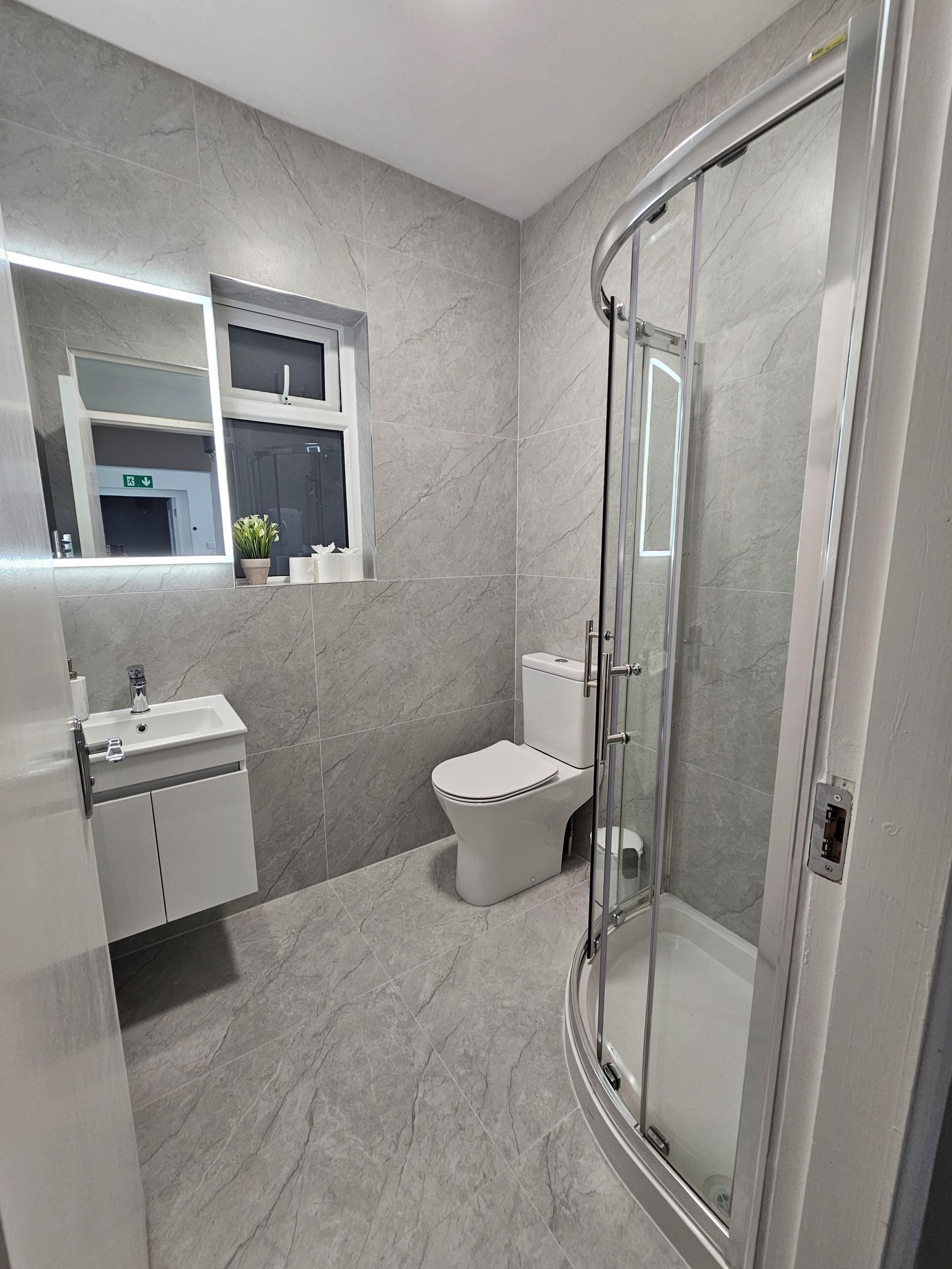A bathroom with a glass-enclosed shower, a toilet, and a sink with a mirror above.