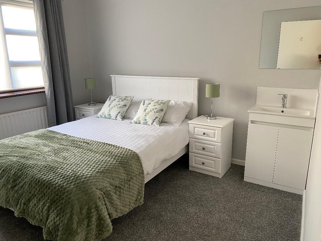 A bedroom with a bed, bedside tables, a dresser, and a window with curtains.