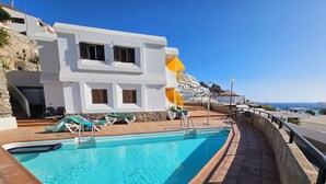 A swimming pool with lounge chairs and a white building with windows and a yellow awning. - Modern Apartment With Sea View With Pool Puerto Rico (Mogan)