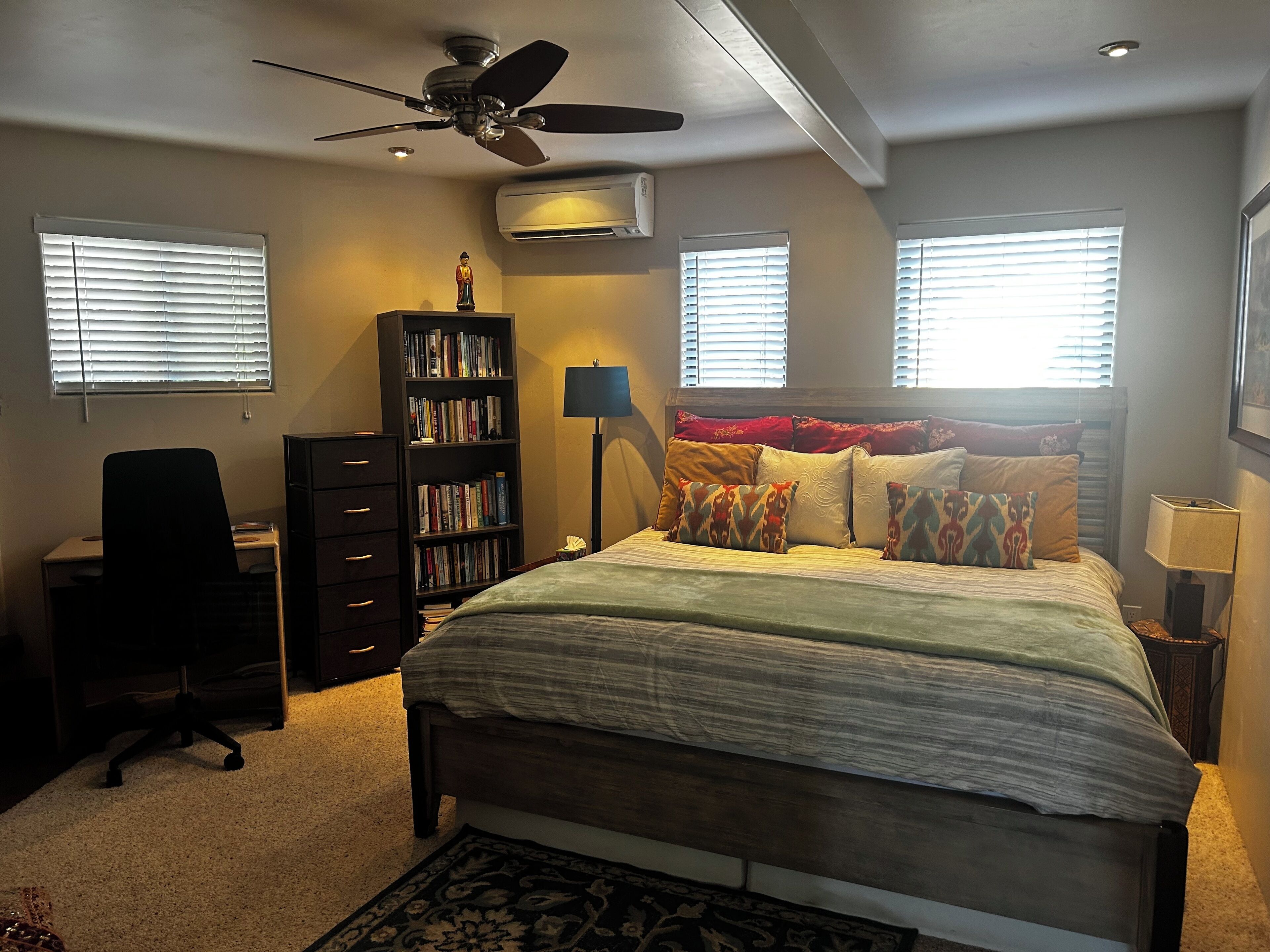 Un dormitorio con cama, escritorio, silla, estantería y ventilador de techo.