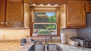 Cocina con encimeras de granito, dos fregaderos de acero inoxidable, armarios de madera, una ventana con vistas a zonas verdes y un salpicadero de azulejos.