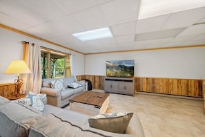A living room with a sofa, coffee table, TV, and wooden paneling.