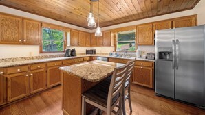 Una cocina con armarios de madera, encimeras de granito, un refrigerador de acero inoxidable y una lámpara colgante.