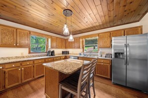 Una cocina con armarios de madera, encimeras de granito, un refrigerador de acero inoxidable y una lámpara colgante.