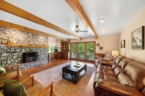 Una sala de estar con chimenea de piedra, vigas de madera, un sofá de cuero y un comedor con mesa y sillas.