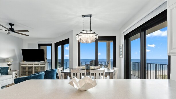 A modern living room with a large dining table, a chandelier, and a view of the ocean.