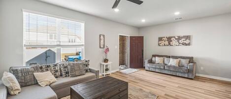 A living room with a sectional sofa, a coffee table, a ceiling fan, and a door leading to another room.