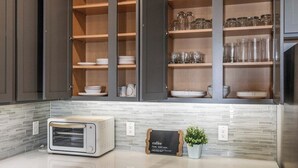 Une cuisine avec des placards ouverts, un grille-pain, un panneau indiquant qu'on y sert du café et une plante en pot.