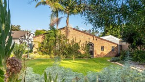 A brick building with a small front yard, surrounded by various plants and trees.