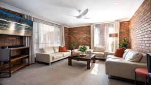 A modern living room with a brick wall, two sofas, a coffee table, and a TV mounted on the wall.