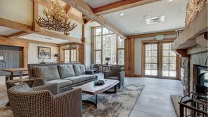 A spacious living area with a fireplace, large windows, and a chandelier.