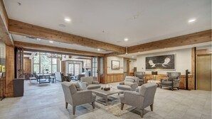 A spacious lobby with a high ceiling, wooden beams, and a central seating area with armchairs and a coffee table.