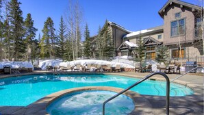A swimming pool with a hot tub, lounge chairs, and a building with a ski lodge in the background.