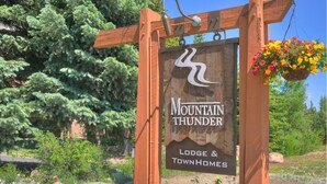 A wooden sign with the text "Mountain Thunder Lodge & Townhomes" and a hanging flower basket.