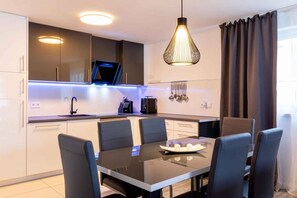 Una cucina moderna con zona pranzo, comprensiva di tavolo e sedie, una lampada a sospensione e una TV sopra il bancone.