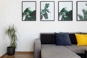 Un salon avec un canapé gris, une plante en pot et quatre tableaux encadrés accrochés au mur.