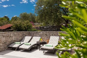 A sunlit outdoor seating area with stone walls and lounge chairs. - Holiday home mit Pool und Terrasse (Vela Luka)
