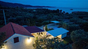 A house with a red roof, a covered patio, and a view of a body of water and hills.