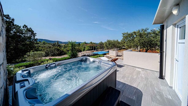 A hot tub with a view of the surrounding landscape, a patio area, and a building with a garage.