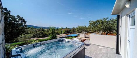 Un bain à remous avec vue sur le paysage environnant, un espace patio et un bâtiment doté d’un garage.