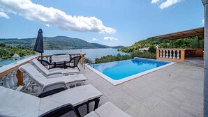 A pool area with lounge chairs and a table, overlooking a lake with mountains in the background. - Holiday home with pool and sea view (Vela Luka)
