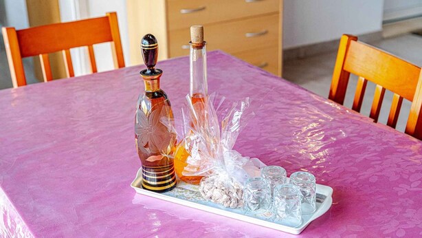 A table with a pink tablecloth, two glass bottles, and a tray with small glass cups and a decorative item. - Holiday home with pool and sea view (Vela Luka)