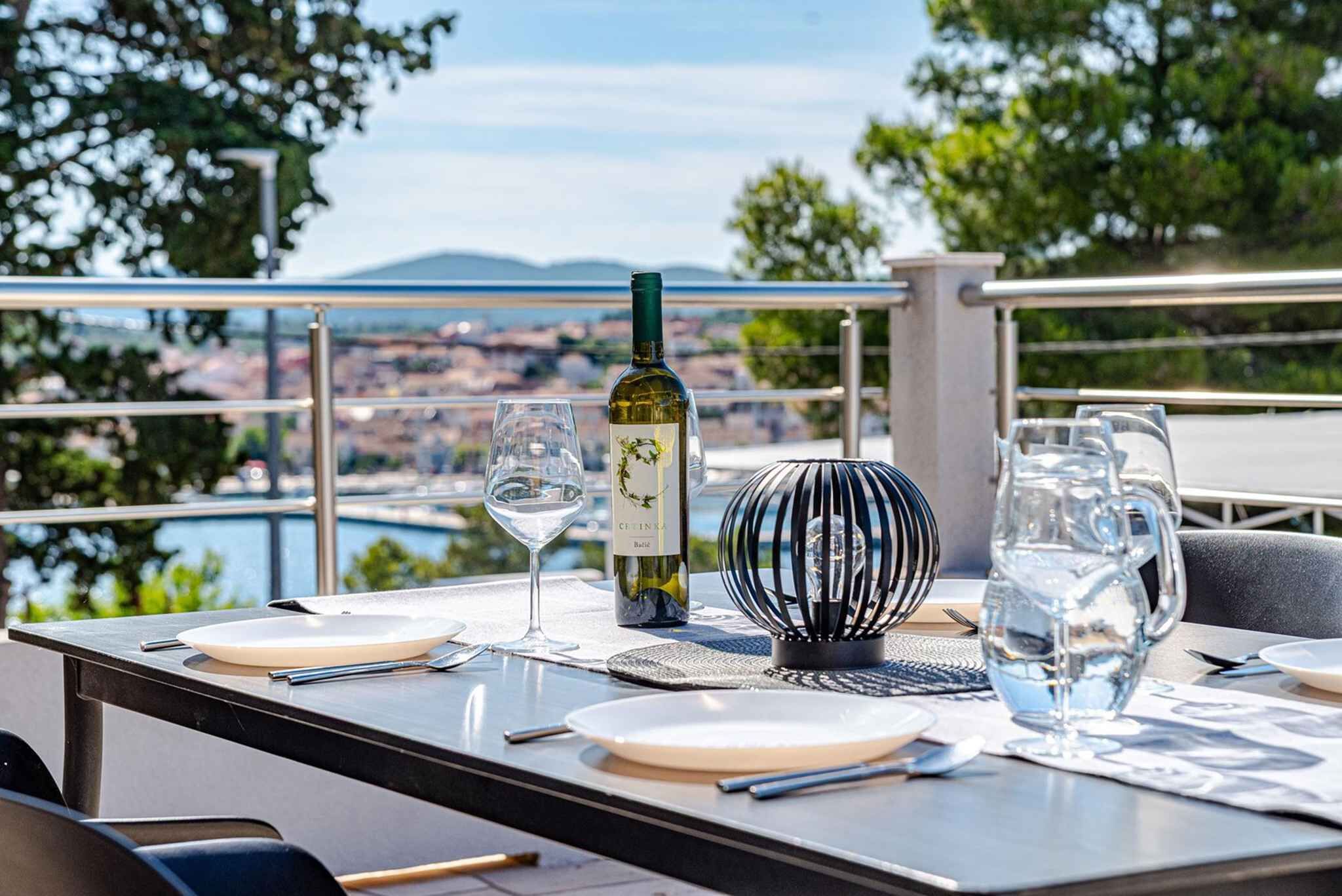 A table set with plates, glasses, a bottle of wine, and a pitcher of water, overlooking a scenic view.