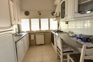 A compact kitchen with white cabinets, a gas stove, a sink, and a window with lace curtains.