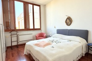 A bedroom with a bed, a window, a radiator, a chair, and a picture on the wall.